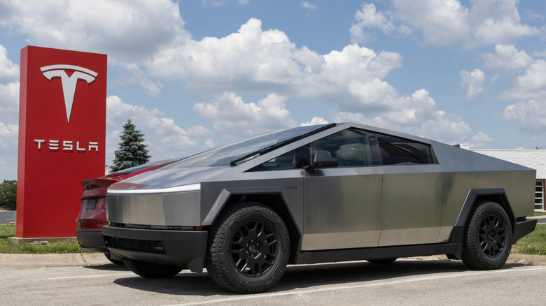 A Cybertruck parked by a Tesla sign