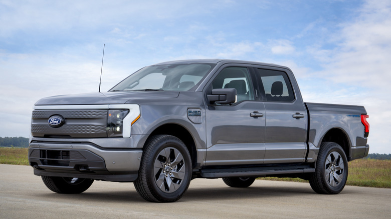 Front 3/4 view of Ford F-150 Lightning in gray on a runway, partially cloudy sky