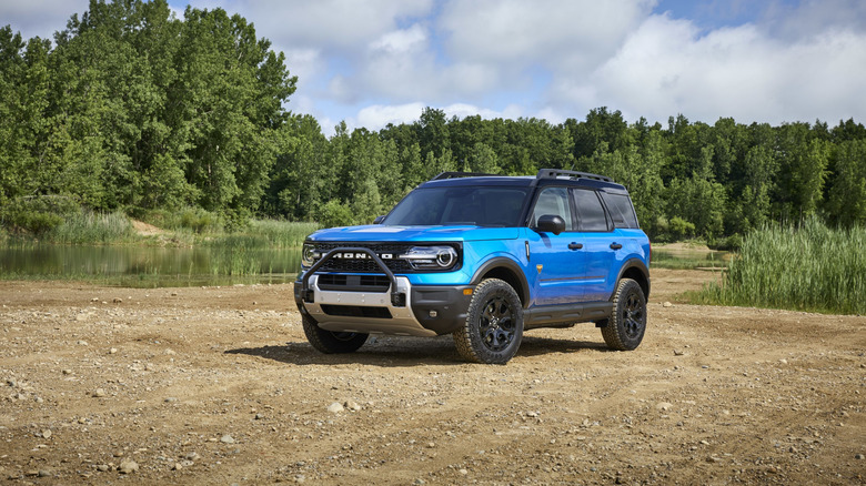 Blue 2025 Ford Bronco Sport SUV seen parked on dirt in front of a pond