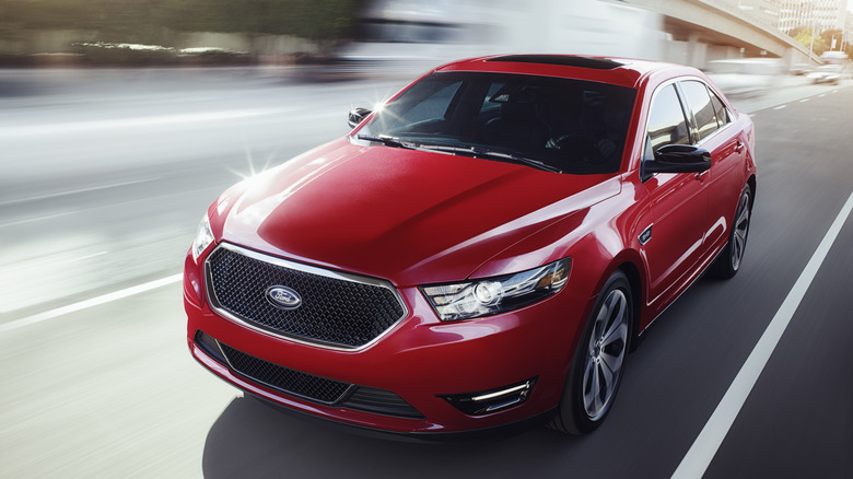 Red 2017 Ford Taurus sedan seen from above left front driving on a city street