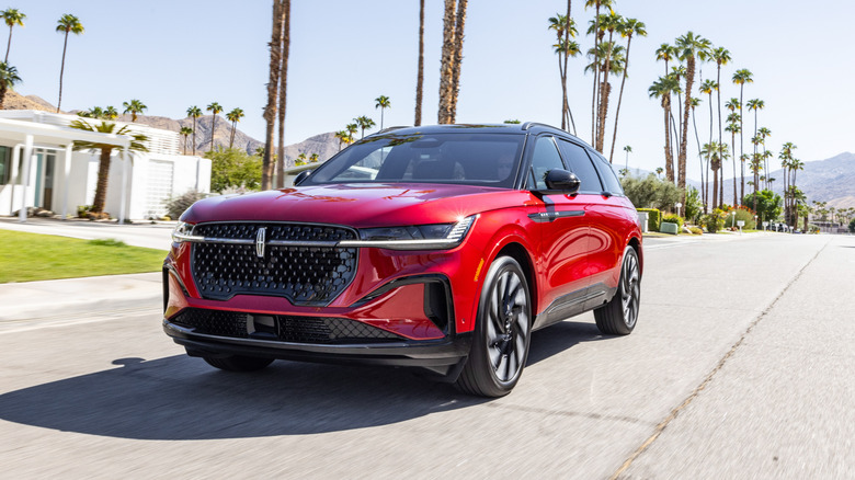 Red 2025 Lincoln Nautilus SUV seen from front left driving on street lined with palm trees