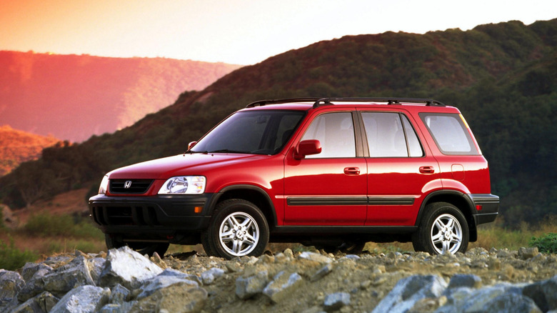 A red first-generation Honda CR-V parked on rocky terrain with hills in the background.