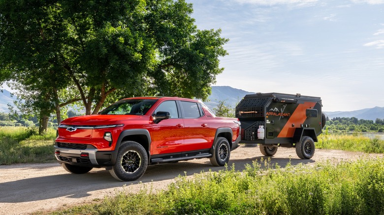 2026 Chevrolet Silverado EV Trail Boss Shown In Habanero Orange Towing A Small Camper