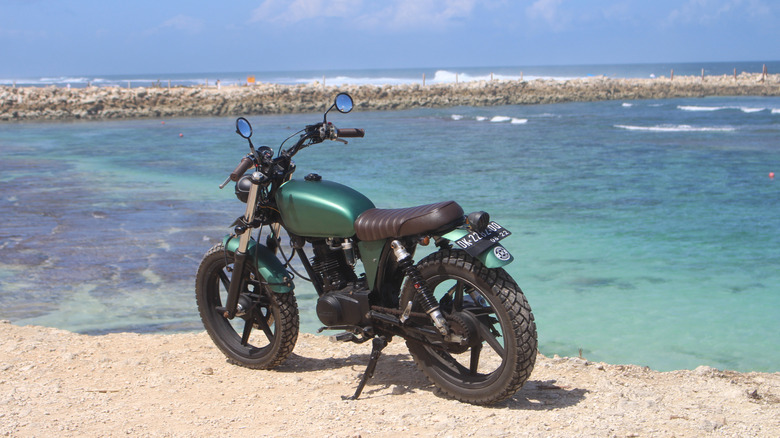 A classic Honda Z50 Monkey parked on the shore of a turquoise blue ocean.