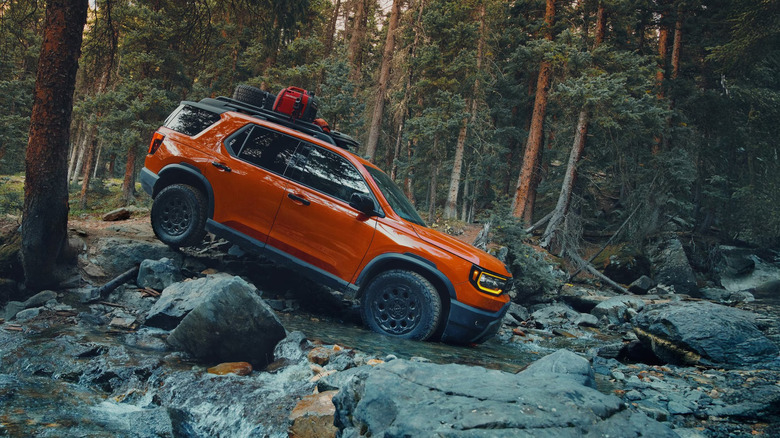 An orange Honda Passport traversing a stream in the woods
