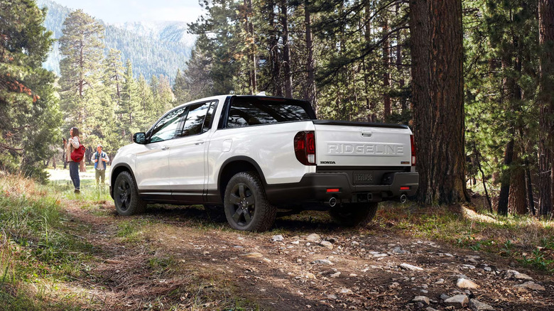 A white Honda Ridgeline parked in the woods next to two hikers