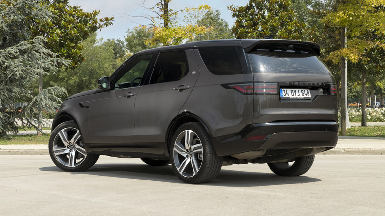 A grey Land Rover Discovery three row parked at the side of a road in a parking lot