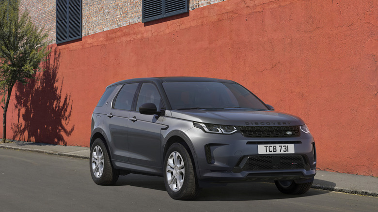 A grey Discovery Sport parked in front of a red wall, front view