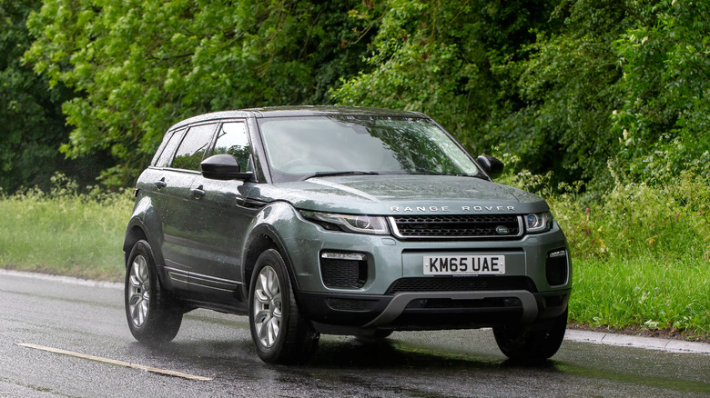 A dark colored Range Rover Evoque moving at speed along a road on an overcast day