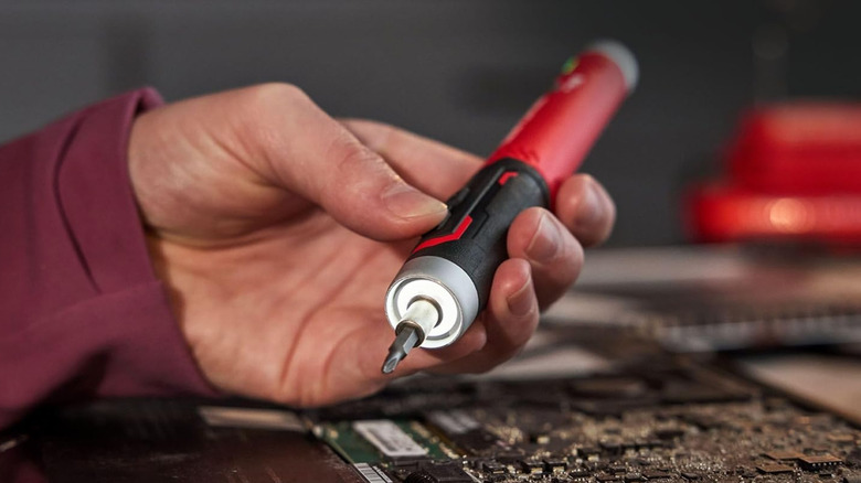 The Craftsman Electric Screwdriver with charging base held in hand over an open laptop.