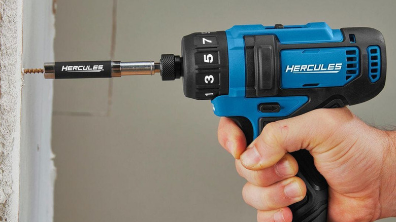 A big Hercules electric screwdriver screwing a screw to a wall.