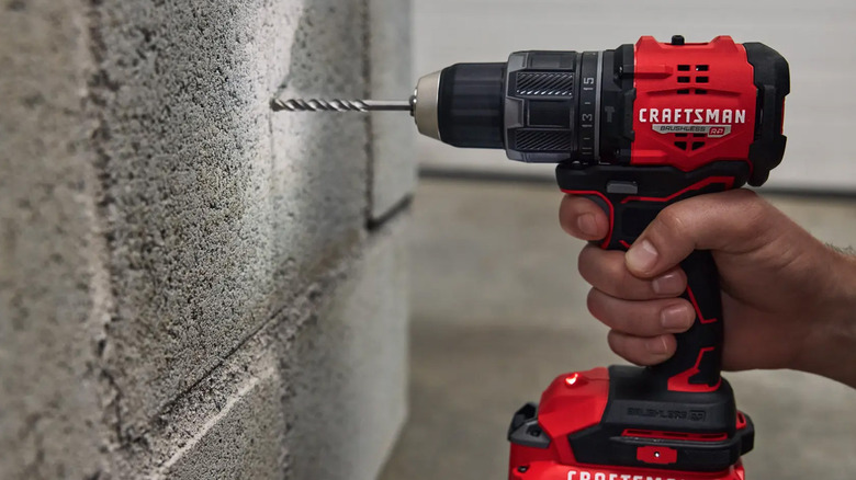 A person drilling a hole into a cinder block wall