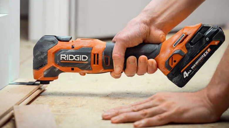 A man using a Ridgid multi-tool to cut a piece of wood
