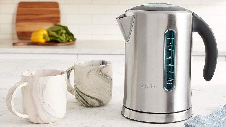 Breville stainless electric kettle on a countertop next to two mugs