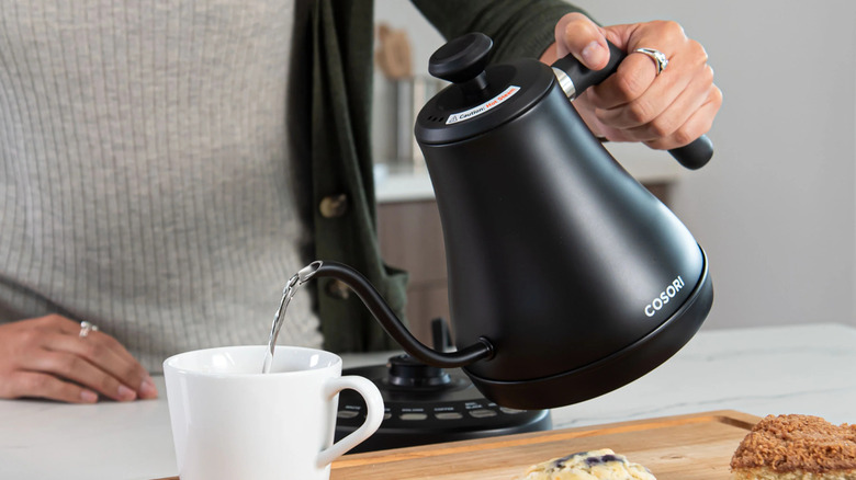 Person pouring water from a black Cosori electric kettle