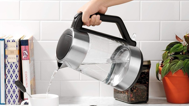 A hand pouring water from an Oxo electric kettle into a cup