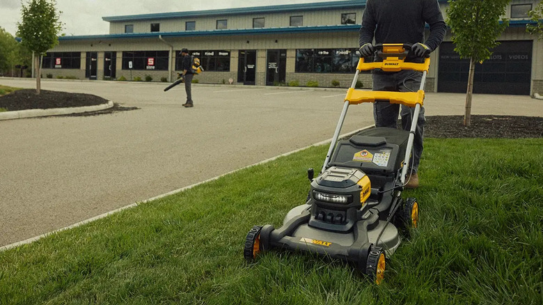 Man pushing DeWalt lawn mower on the grass with a building behind him