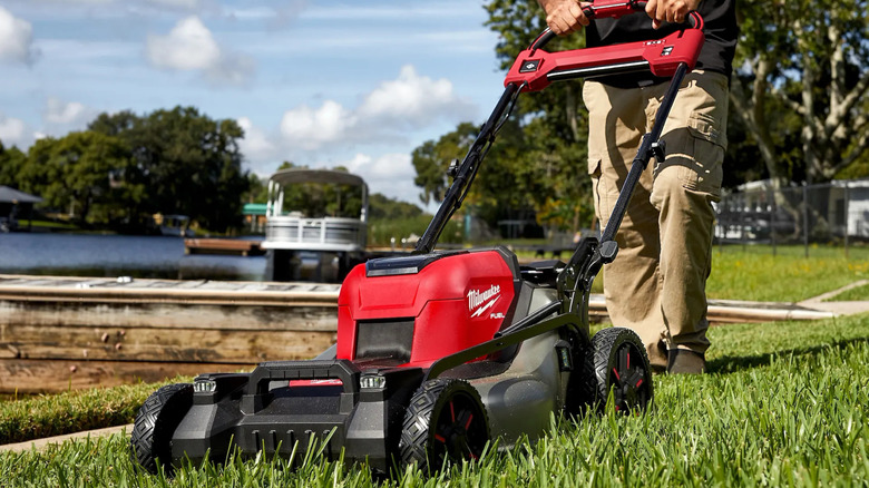 Milwaukee lawn mower being pushed on a lawn next to a lake