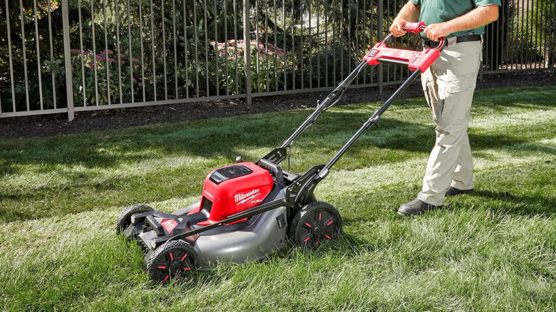 Milwaukee lawn mower being pushed on a front lawn with tall grass