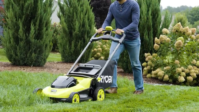 Ryobi lawn mower being pushed by someone on a lawn with tall grass