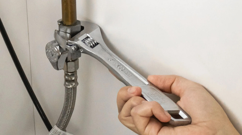A person tightening a nut on a water line under a sink.