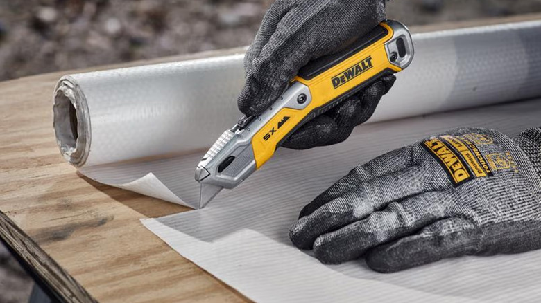 A person in gray gloves cutting foam with a DeWalt utility knife