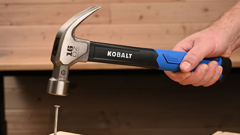 A man using a Kobalt hammer to drive a nail into wood