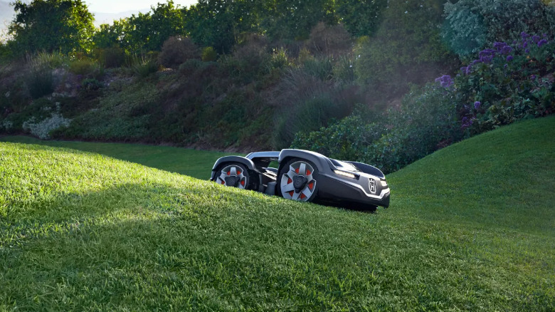 A Husqvarna Automower 435X AWD crawling on a small hill in a yard.