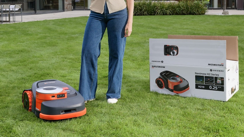 A person standing next to a Segway Navimow H2 robot mower on a lawn.