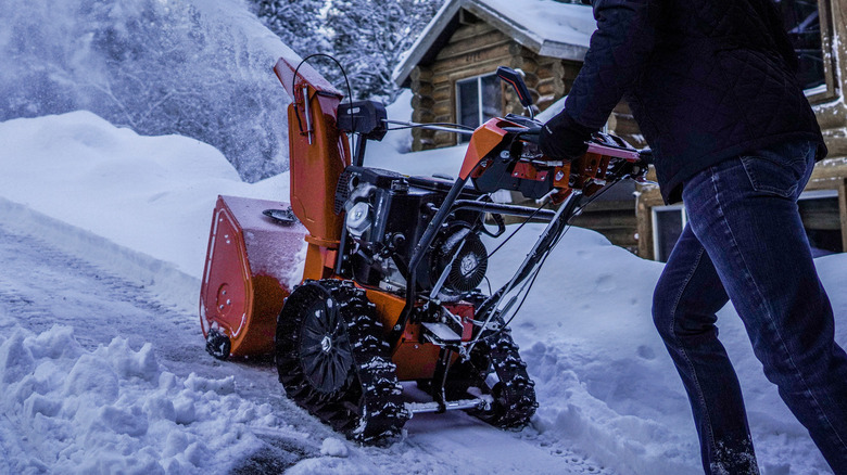 A person pushes an Ariens snow blower uphill in the snow