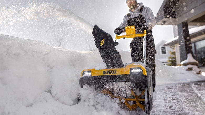 A person operating a DeWalt snow blower in front of a house