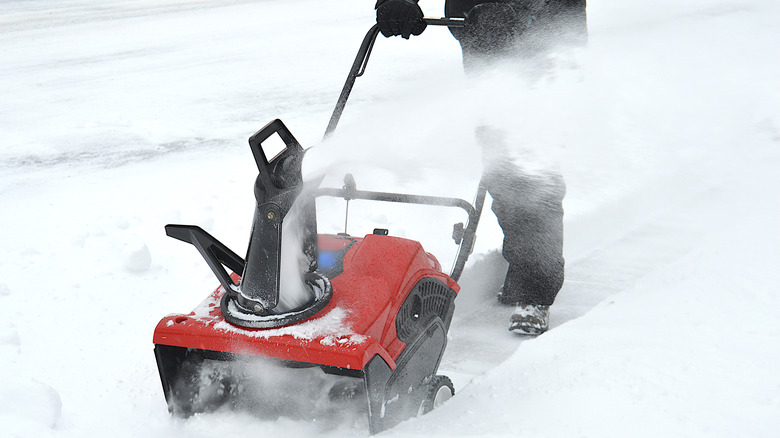 A red snow blower with not brand name visible being pushed by a person off camera