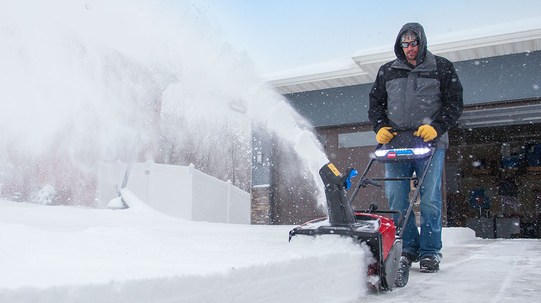A person uses a Toro snow blower in front of a house