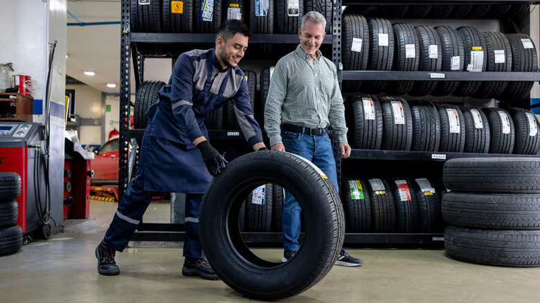Tire technician rolling a tire in front of man
