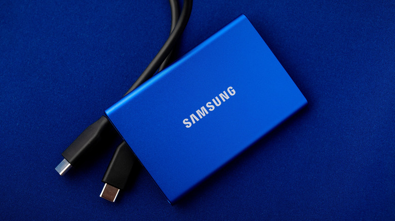 A blue Samsung SSD sits on a blue background beside two black USB-C cable connectors.
