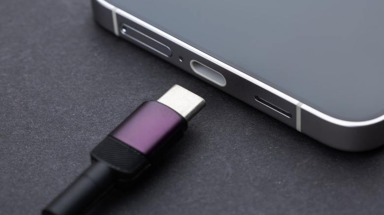 A USB-C cable is positioned beside the charging port of a smartphone on a dark surface.