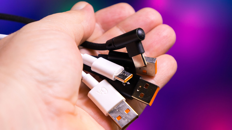 A hand holds five charging cables with different connector types, including USB-A and USB-C.