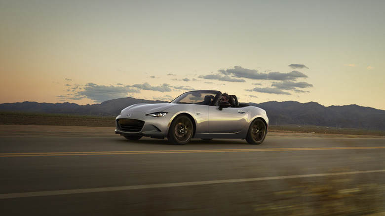 A silver Mazda MX-5 Miata sports car traveling down a highway, front 3/4 view