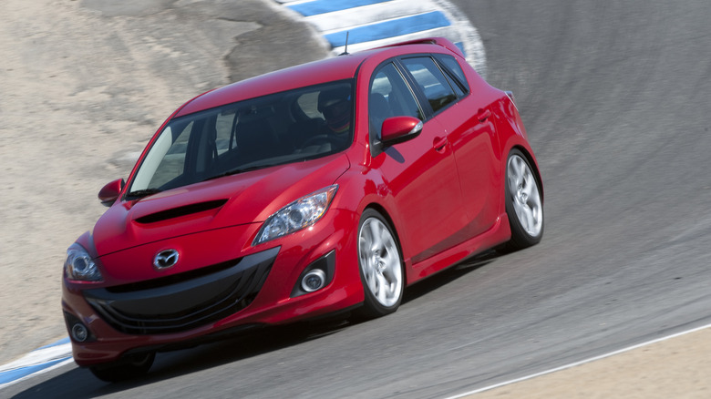 Red 2010 Mazdaspeed3 on race track, front 3/4 view, tilted camera