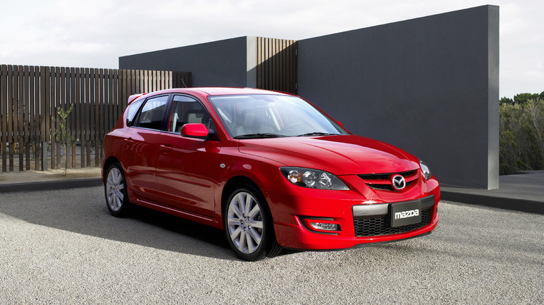 A 2007 Mazdaspeed3 in red parked outside some modern architecture, front 3/4 view