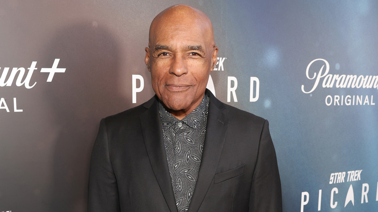 Michael Dorn posing for a picture in a grey jacket and dark shirt