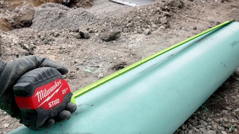 Person measuring pipe with tape measure
