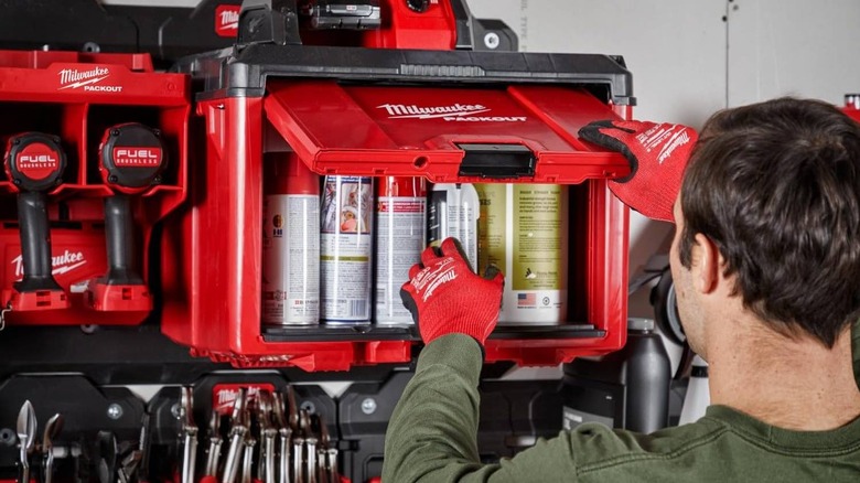 A Packout Cabinet mounted on a wall is being opened, it contains various spray cans.