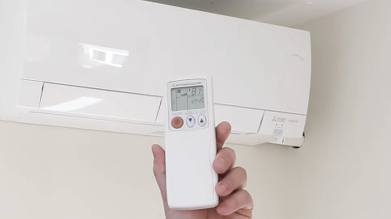 A person holding Mitsubishi mini split remote in front of the AC
