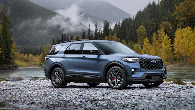 Blue 2025 Ford Explorer ST SUV parked by a river with mountains in the background, seen from right front
