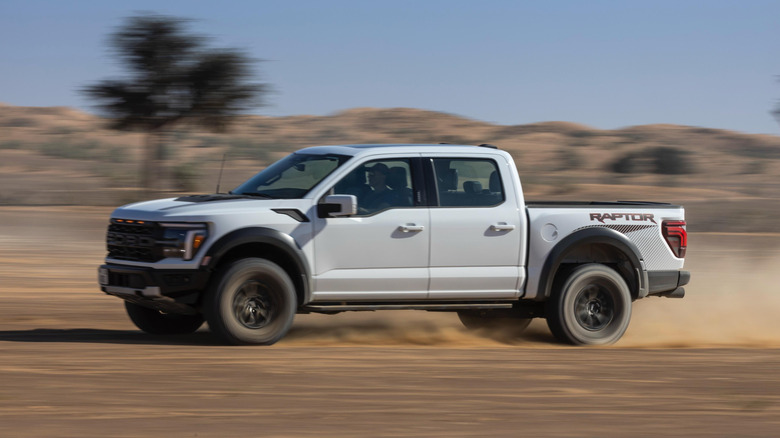 White 2025 Ford F-150 Raptor pickup truck seen from the left driving in the desert
