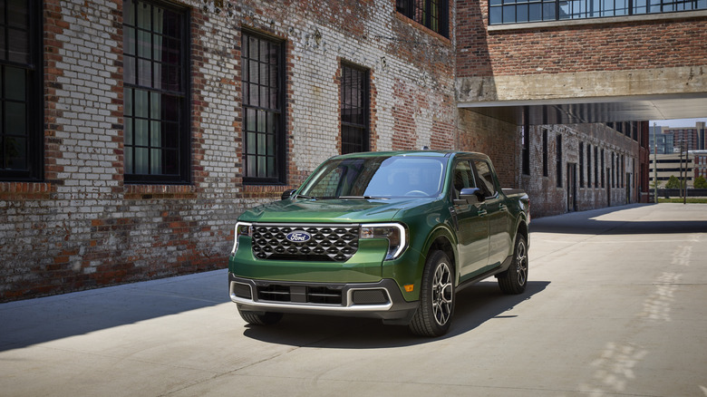 Green 2025 Ford Maverick pickup driving through industrial neighborhood seen from front left
