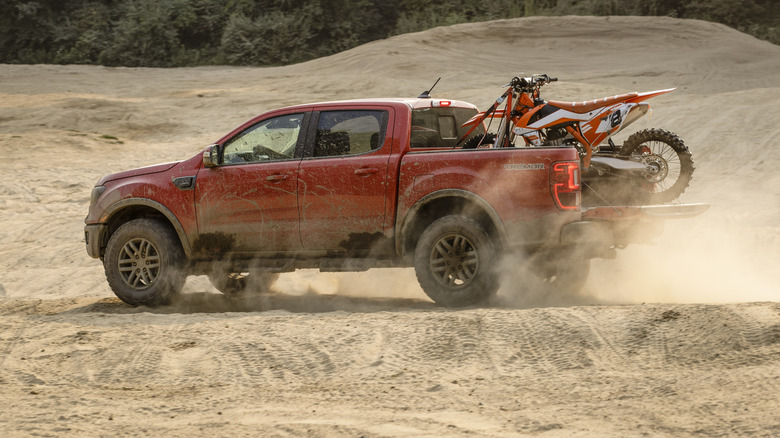 Red Ford Ranger Tremor Lariat pickup truck carrying a motorcycle off-road, seen from the left