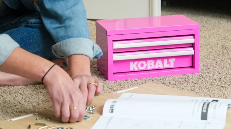 A person uses a pink Kobalt mini 2-drawer toolbox on the floor