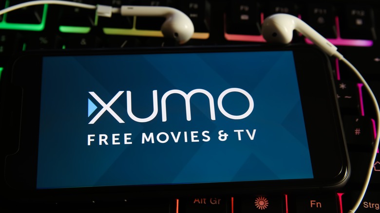 Xumo logo on smartphone with earbuds and a backlit kekyboard